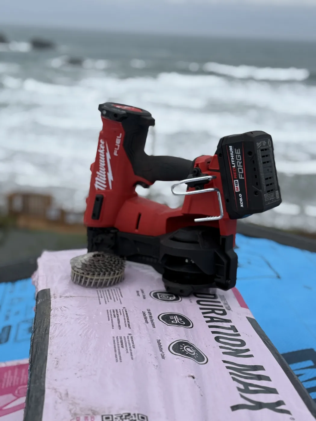 A roofing nailer and a coil of nails on synthetic underlayment, surf behind