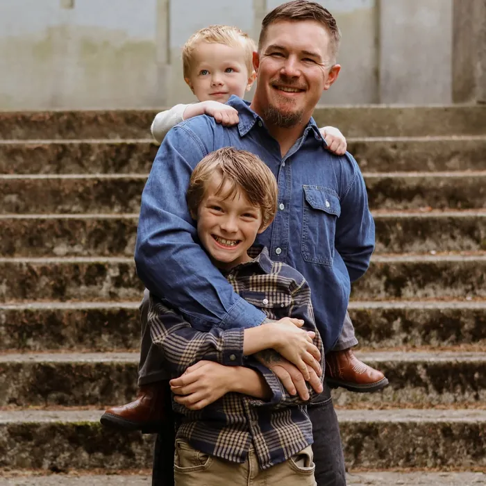 Zachery Kingston smiling with his two sons in front of him on a set of old concrete steps